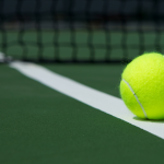 lime green tennis ball laying on a tennis court